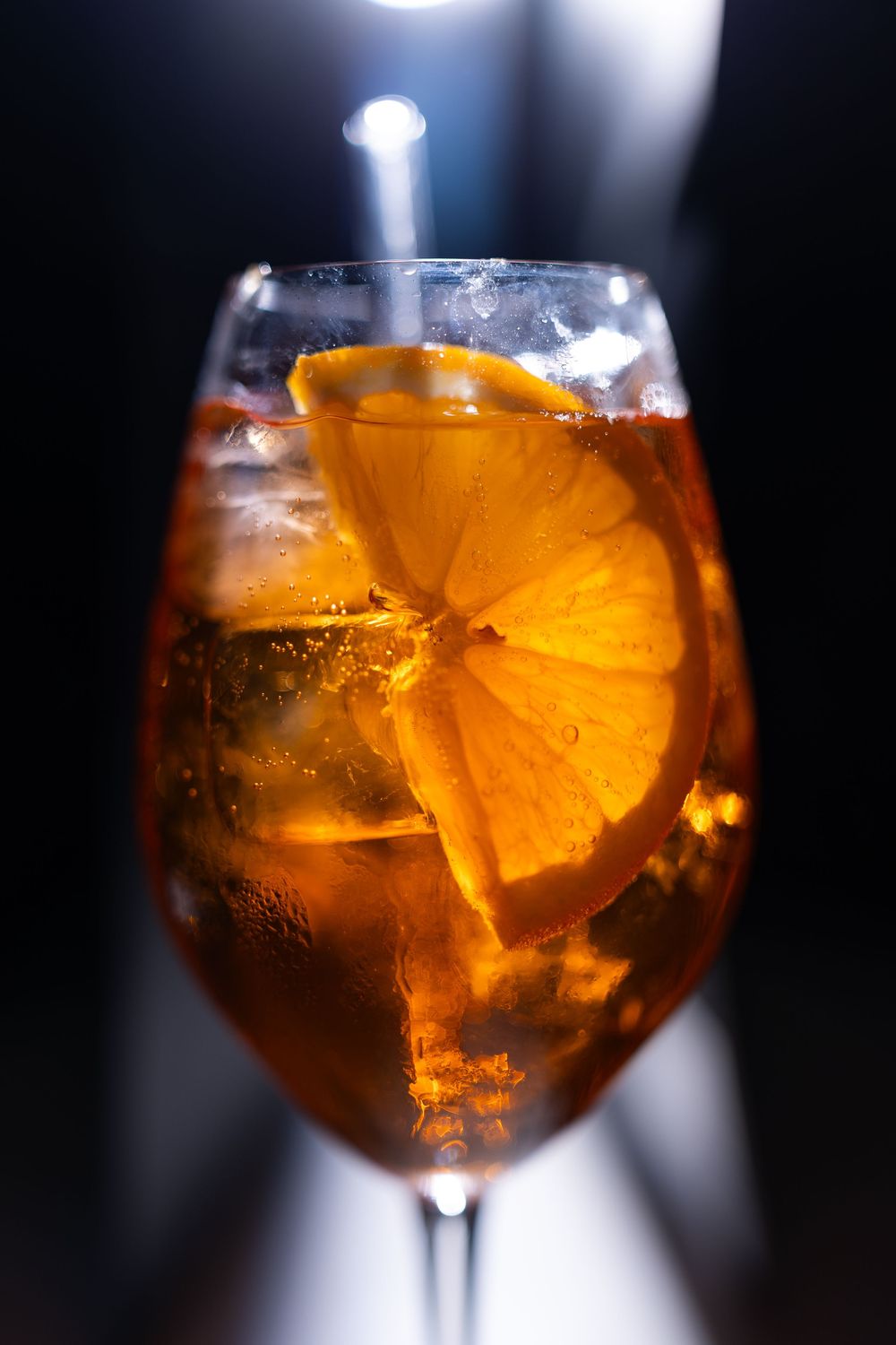 A chilled Aperol Spritz cocktail in a wine glass with orange slices and ice on a dark background.