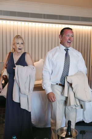 Couple reacts with surprise and laughter in hotel room with champagne bucket during wedding celebration.