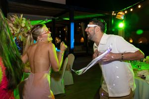Couple dancing energetically at tropical wedding reception under colorful green and purple lights.