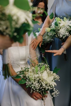 Bride in white lace dress and bridesmaids in blue gowns holding elegant white floral bouquets with greenery at a wedding.