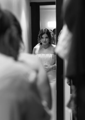 Bride in white strapless gown reflected in mirror during wedding preparations in black and white photo.