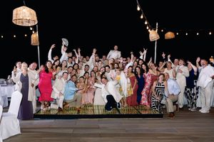Large wedding group photo outdoors at night with string lights, guests celebrating joyfully on a terrace.