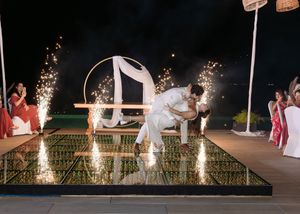Couple sharing romantic dip kiss on mirrored dance floor with sparklers at elegant outdoor wedding reception at night.
