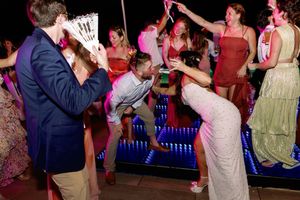 Wedding guests dancing and celebrating energetically on illuminated dance floor at evening reception.