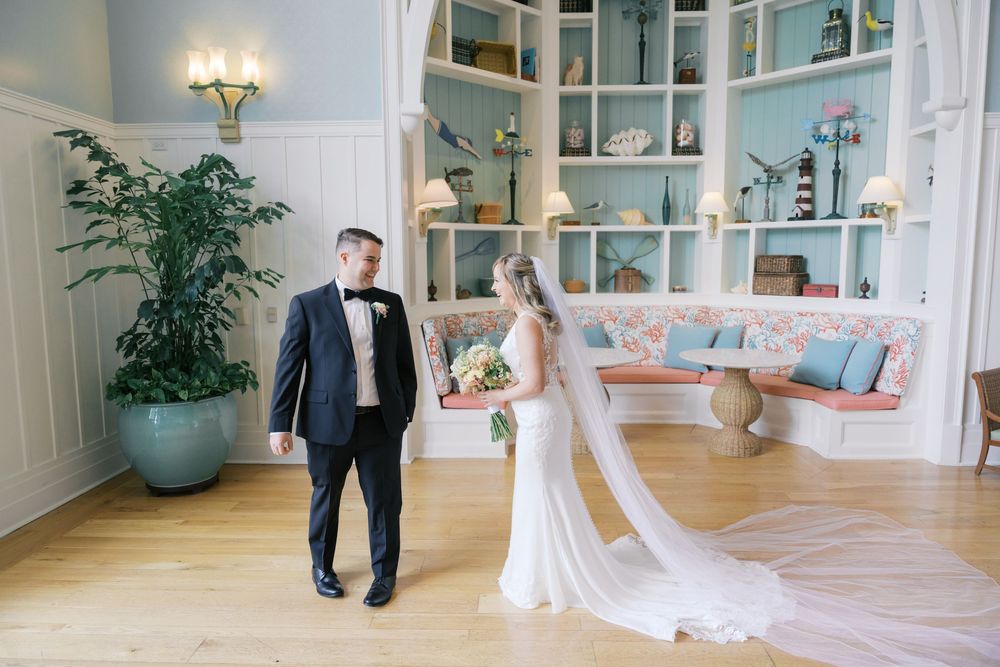 Bride and groom share a first look moment in an elegant coastal-themed venue with blue shelving and hardwood floors.