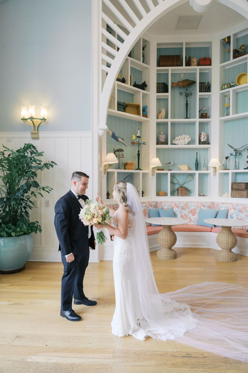 Bride and groom share a tender first look moment in an elegant coastal-themed venue with blue shelving and hardwood floors.
