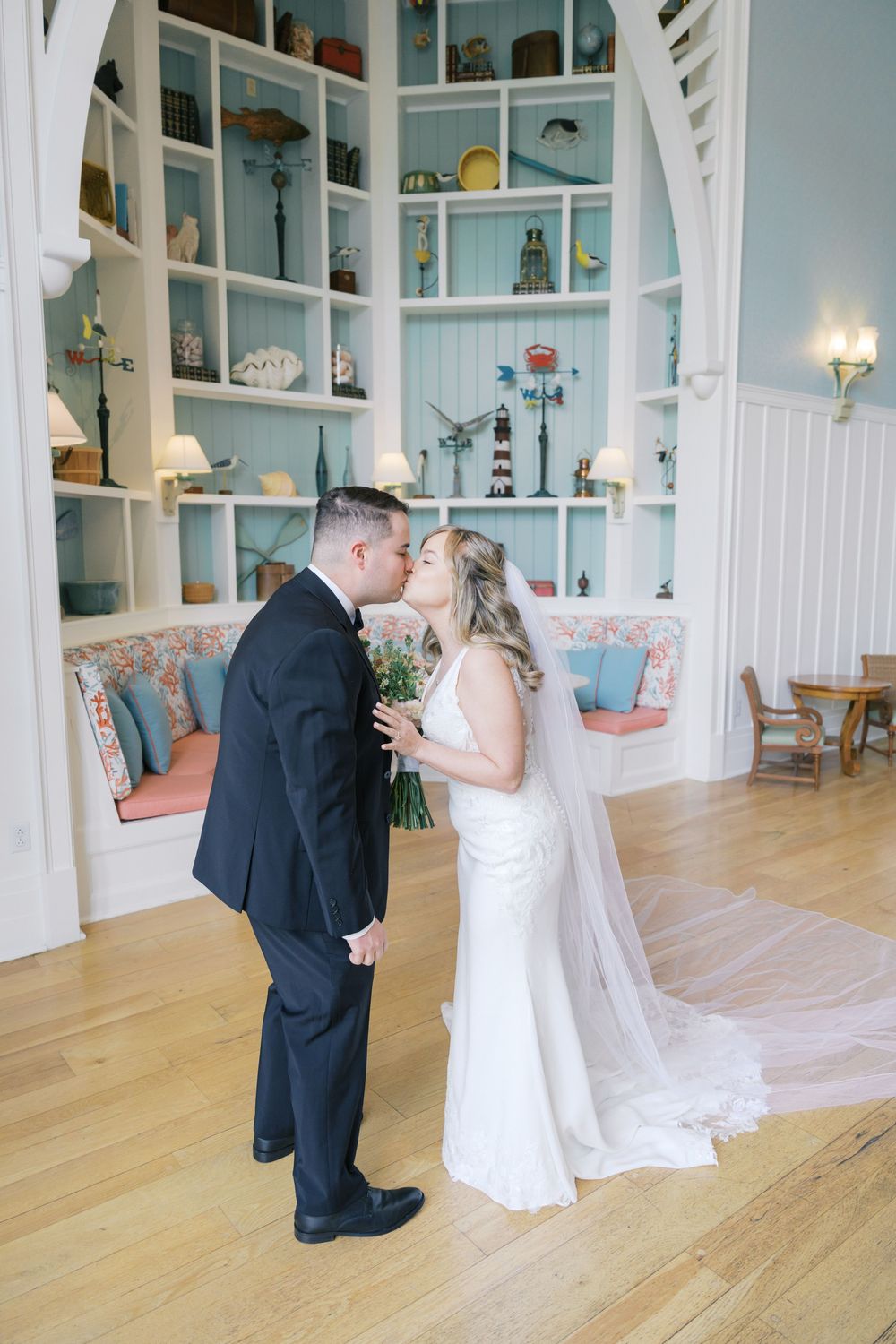 Bride and groom share a kiss inside an elegant coastal-themed venue with blue shelving and hardwood floors.