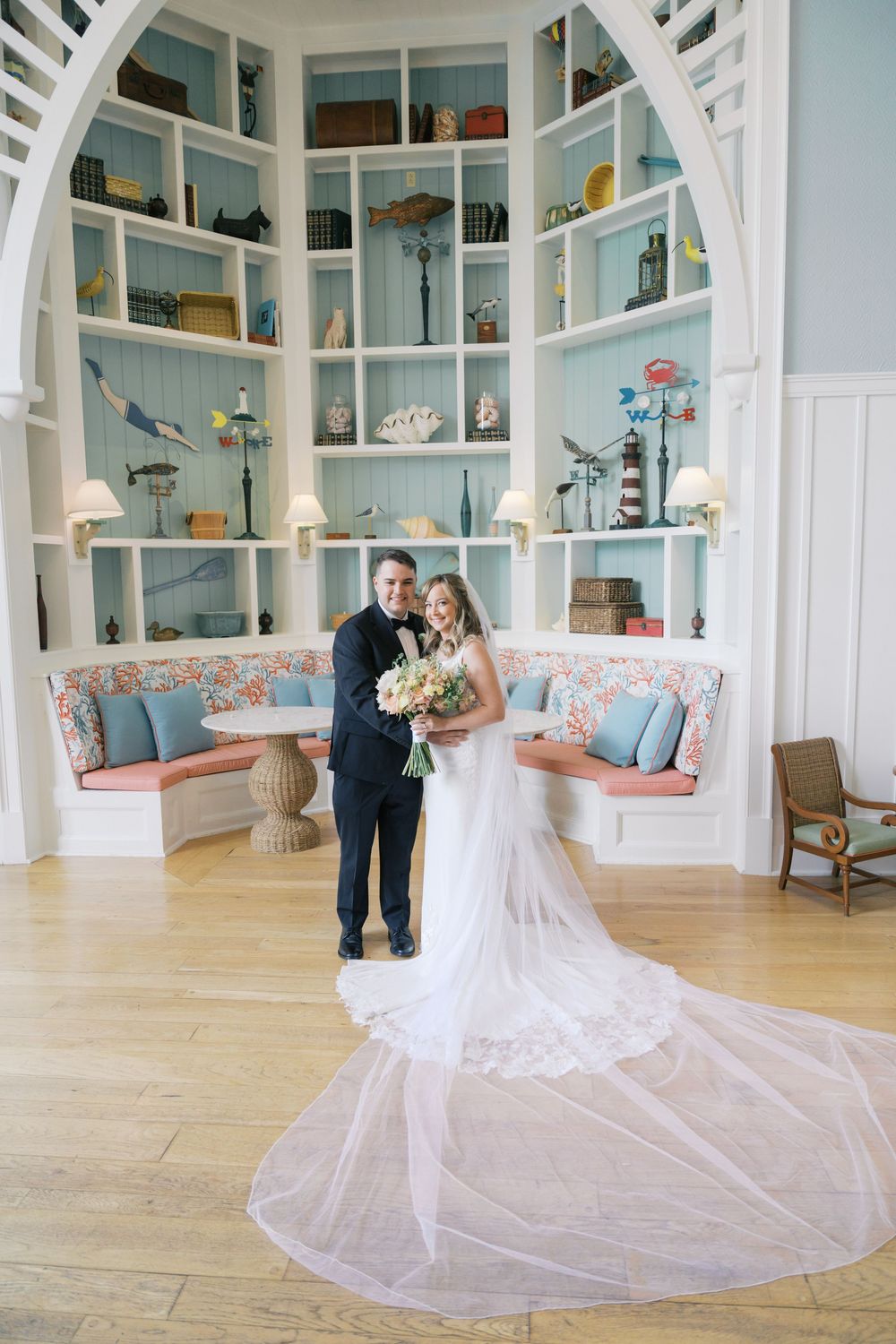 Bride and groom pose in a nautical-themed room with blue shelving and lace wedding gown train.
