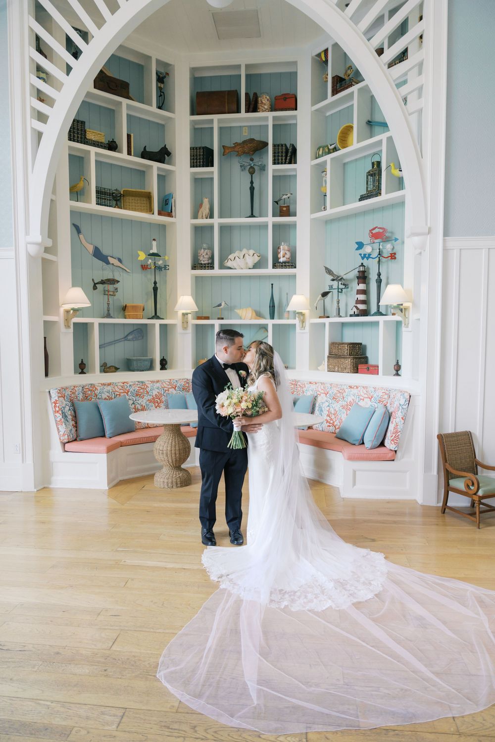 Bride and groom share a kiss inside an elegant arched room with blue built-in shelves and floral decor.