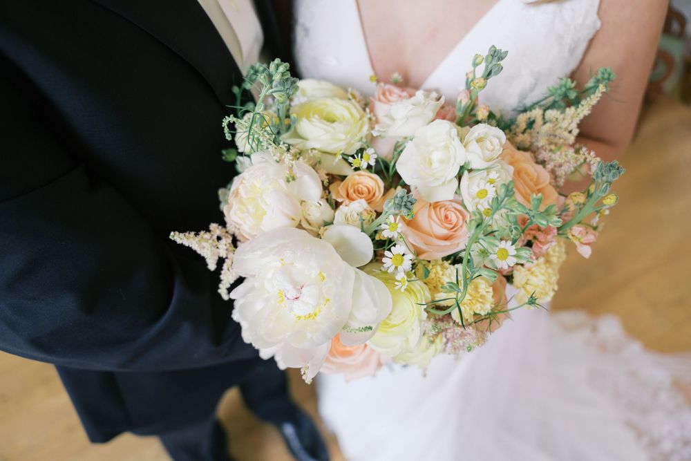 Close-up of a bridal bouquet featuring white peonies, peach roses, and soft greenery accents.
