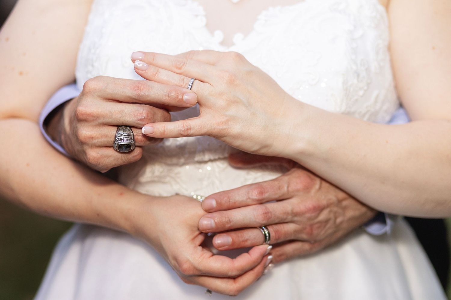Close-up of bride and groom hands showing wedding rings, bride in white lace dress, romantic wedding ceremony detail.