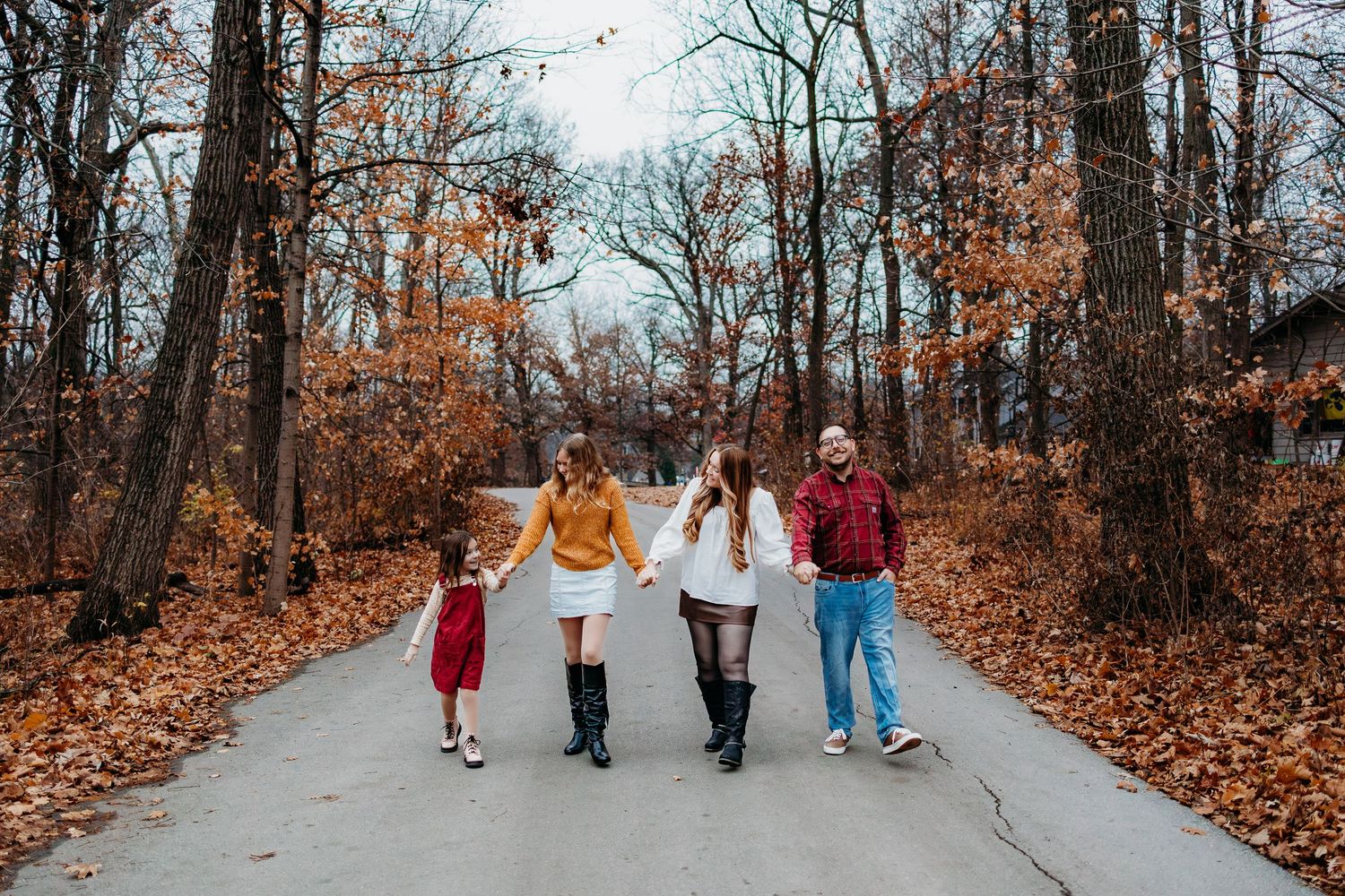 A family of 4 walking together down a path and there leaves on the ground. They are all smiling and laughing.