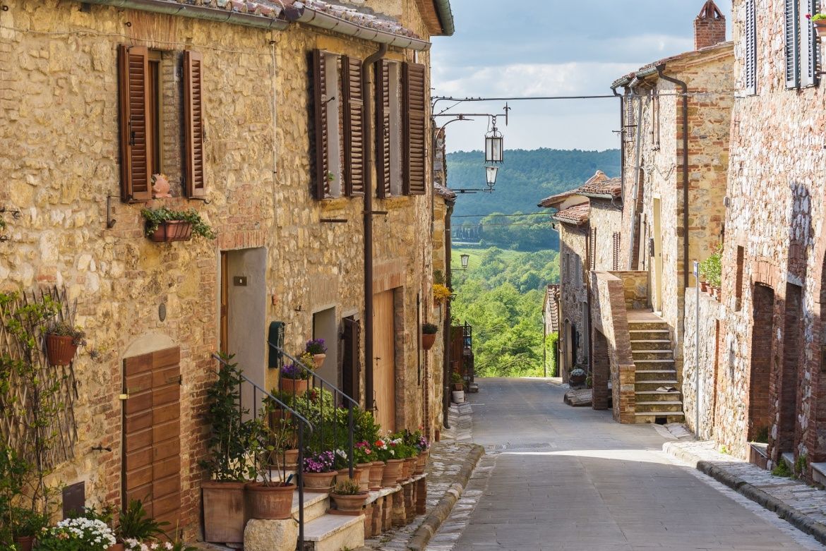 Charming narrow cobblestone street lined with rustic stone buildings and flower pots in a Tuscan hilltop village, Italy.