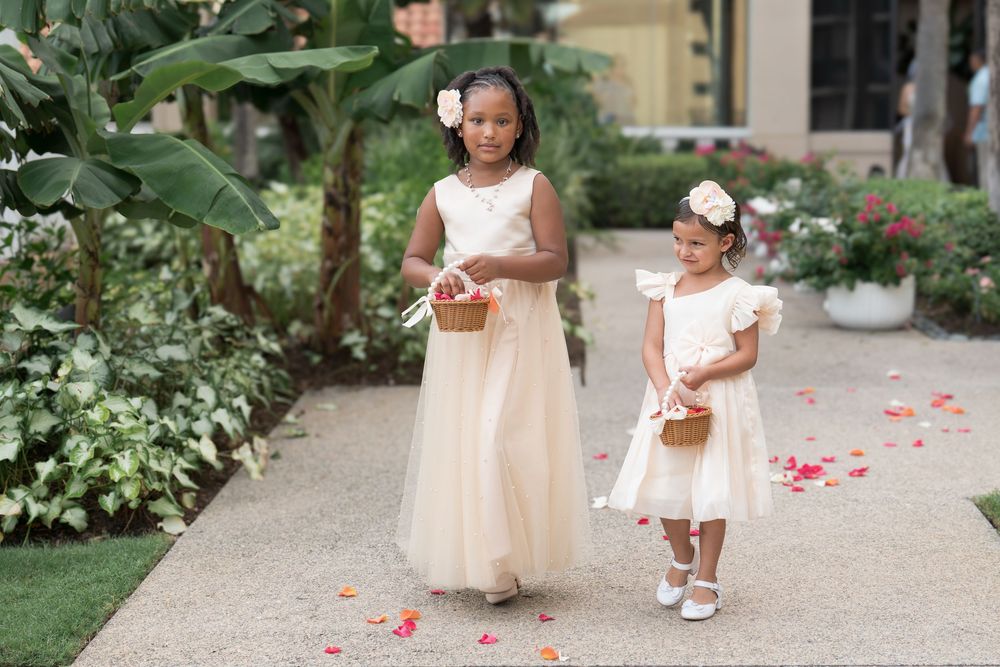 Two flower girls in champagne dresses scatter rose petals down wedding aisle.