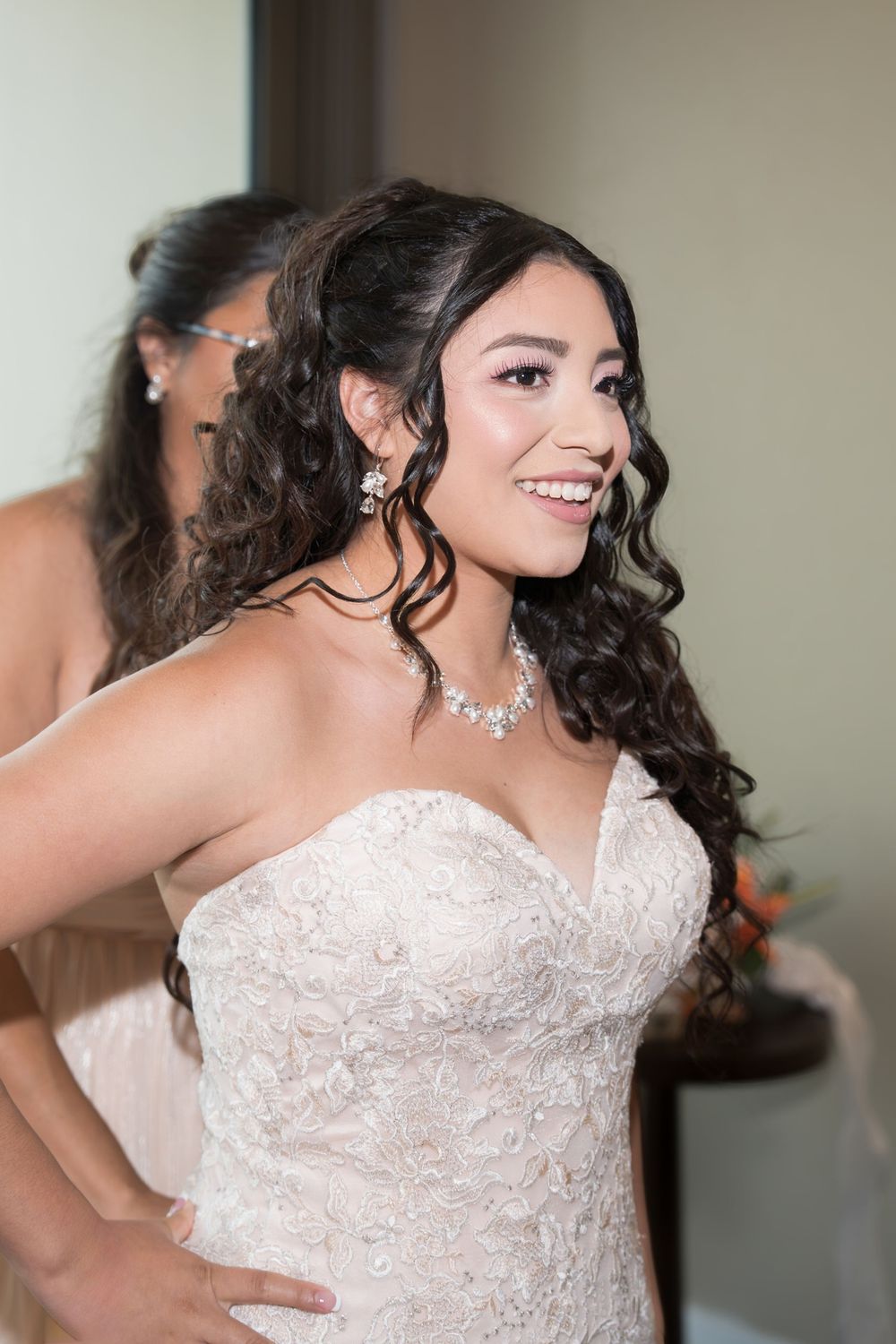 Beautiful bride with curly hair smiling in strapless lace wedding gown with diamond jewelry.