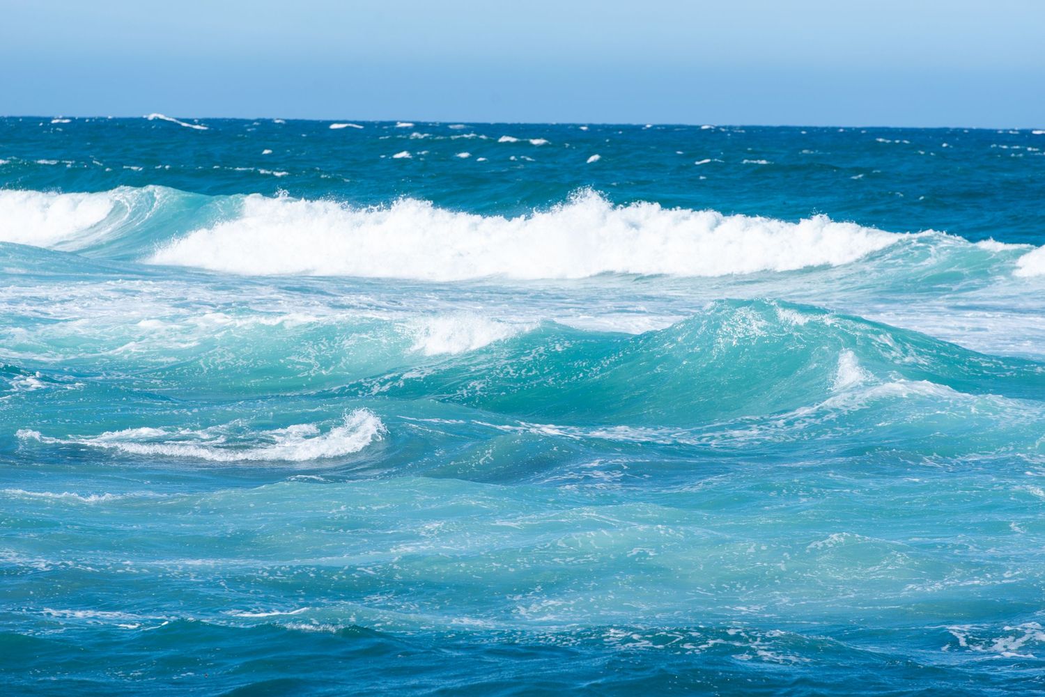 Vibrant turquoise ocean waves crashing in the sea under a clear blue sky.