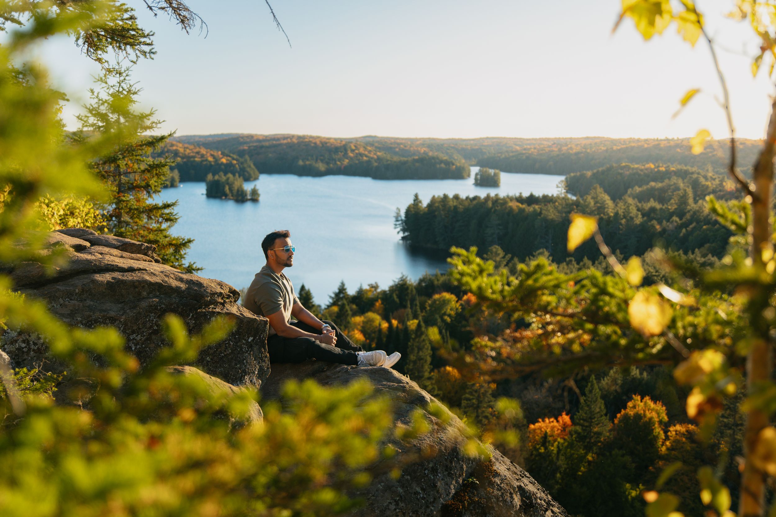 Akash Patel sitting on a rocky lookout over a lake surrounded by fall colours