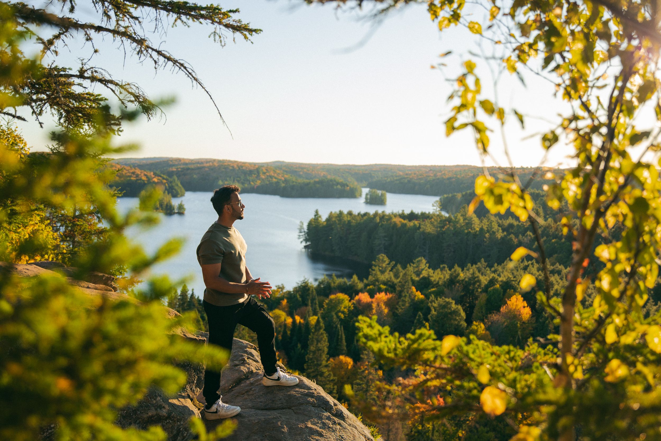 Akash Patel, Toronto wedding photographer, standing on a rocky lookout above a lake in fall