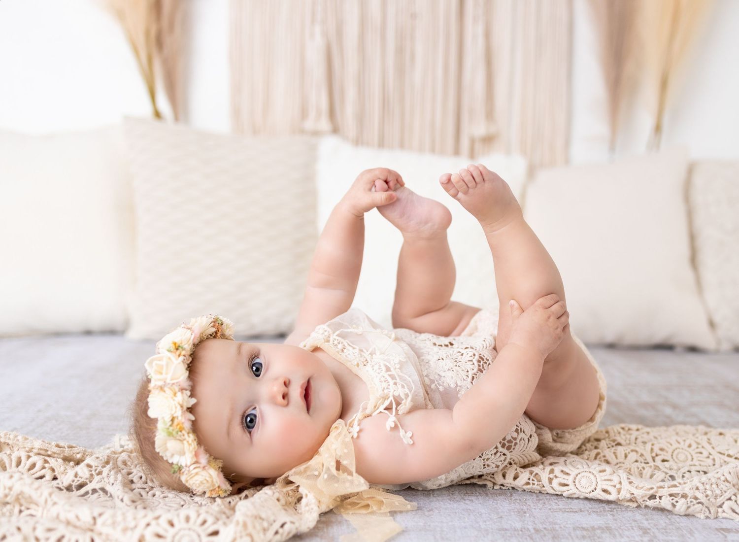 Smiling baby in green outfit lying on white blanket during professional newborn photography session.