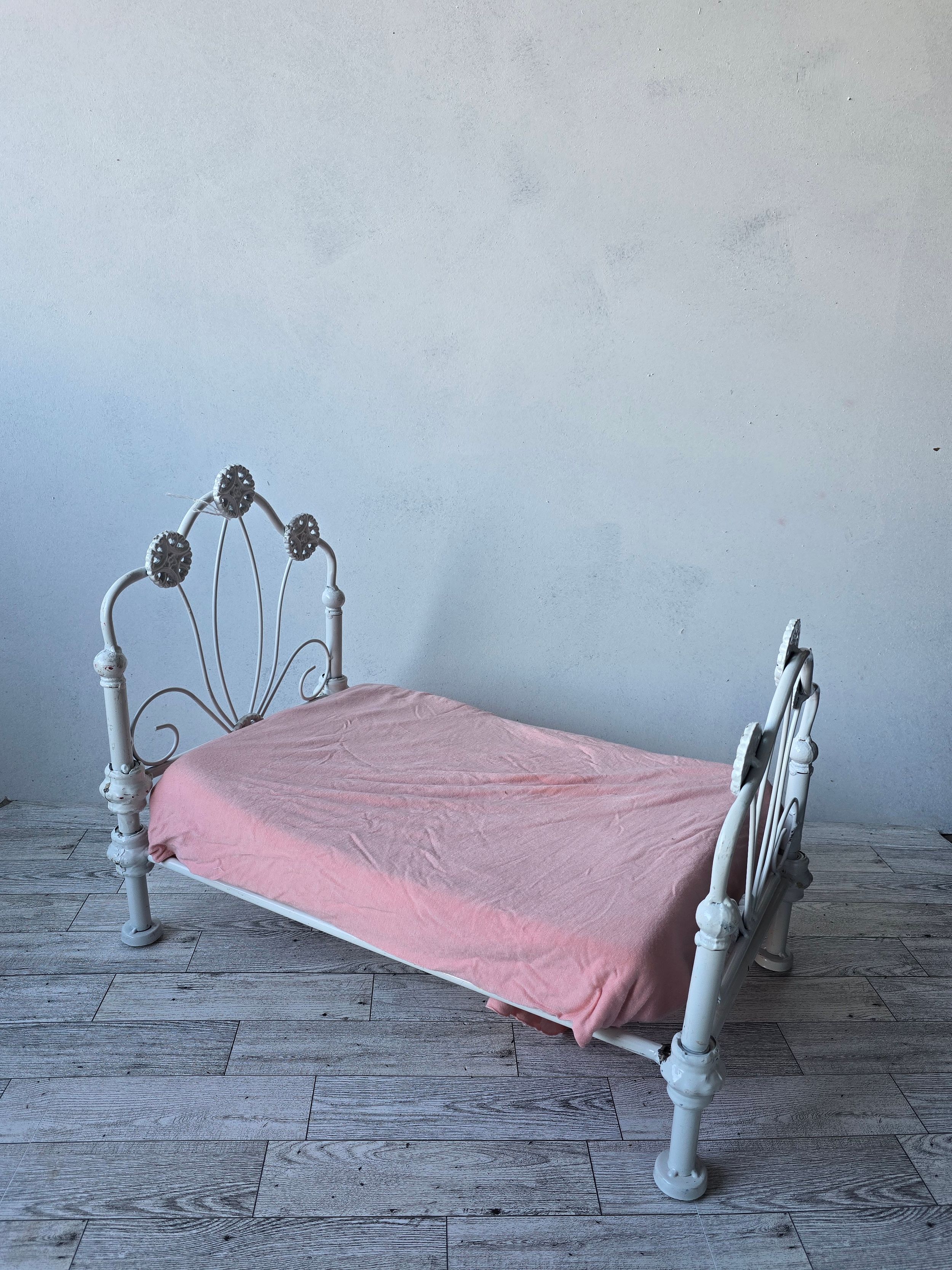 Vintage white wrought iron single bed frame with ornate details and pink bedsheet on wooden floor.