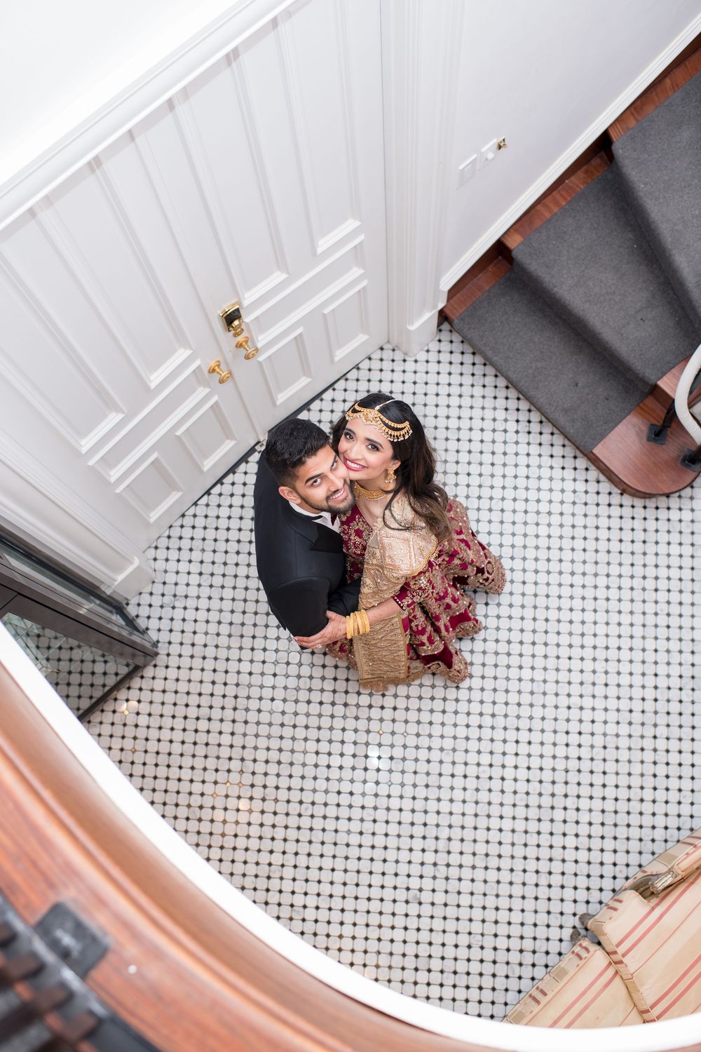 Aerial view of South Asian bride and groom embracing on black and white mosaic tile floor.