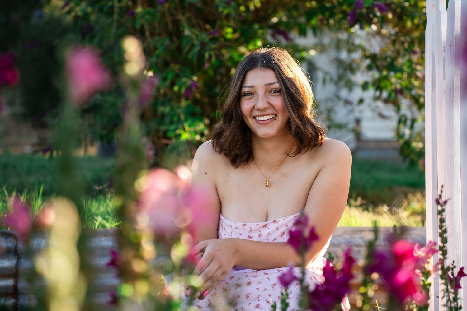 close up portrait of a senior girl amongst pink flowers and by a white picket fence