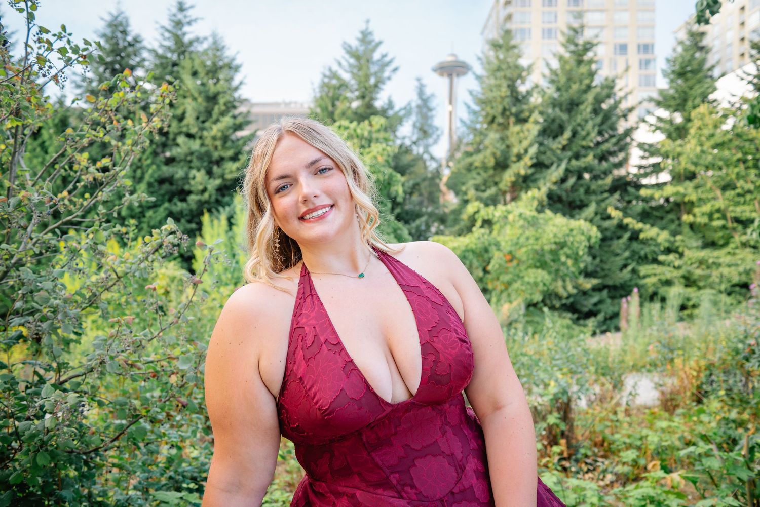 Smiling high school senior surrounded by greenery at Olympic Sculpture Park with Space Needle in the background.