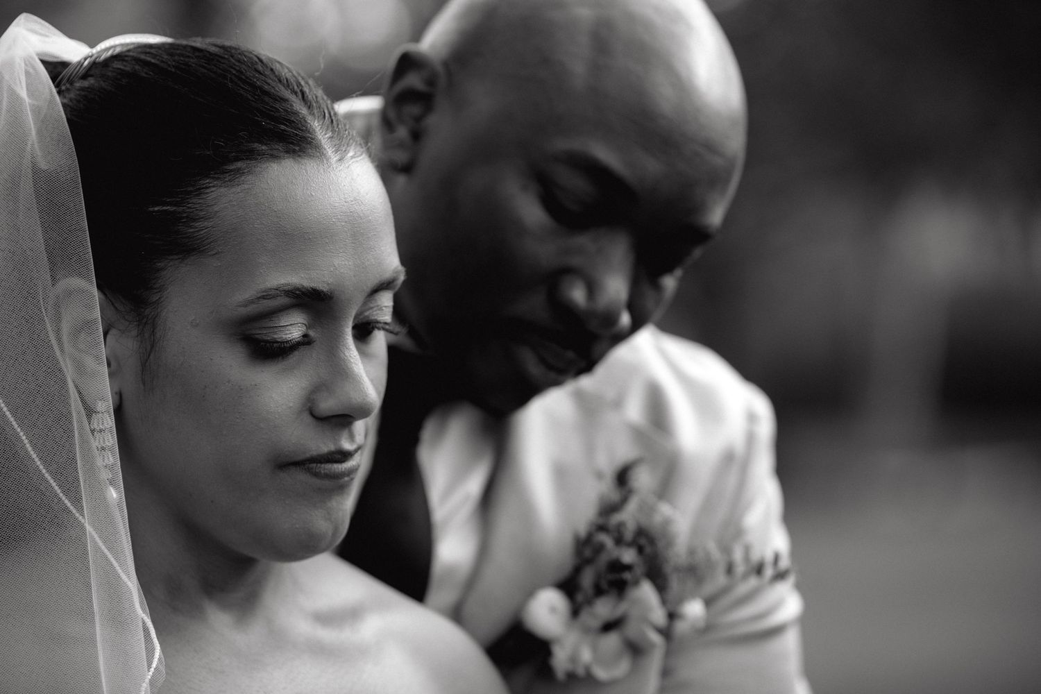 Joyful bride and groom laughing together outdoors, groom in grey suit, bride in white off-shoulder gown at wedding.