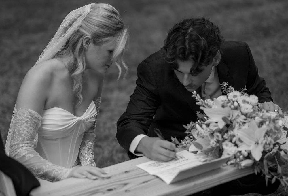 Bride and groom signing wedding documents at outdoor ceremony, black and white photo.
