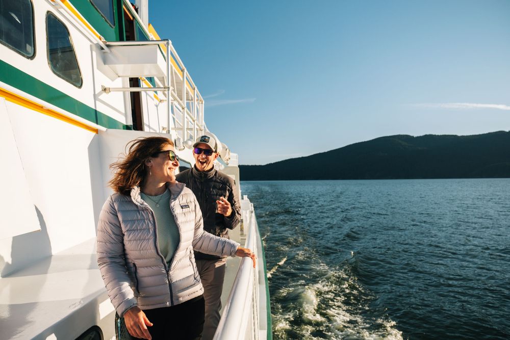 Passengers enjoying the view from a ferry boat deck while cruising on calm waters near mountains.