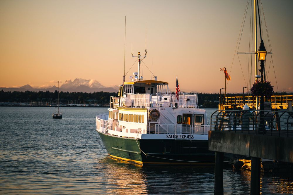 Passenger ferry boat docked at pier during golden sunset with mountains in background and calm water.