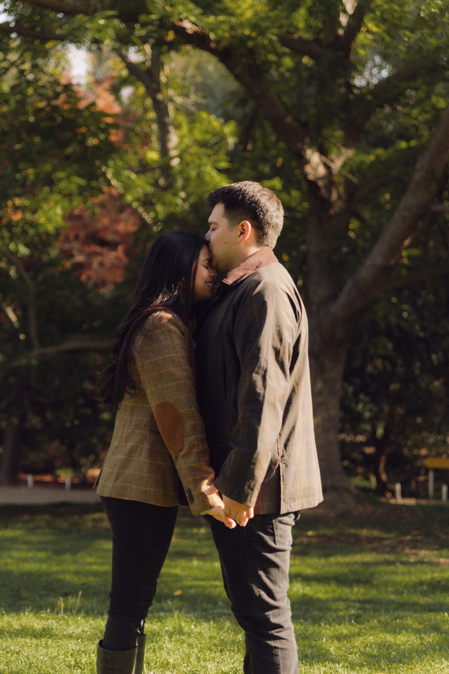 Romantic couple holding hands and embracing tenderly in a lush green park setting.