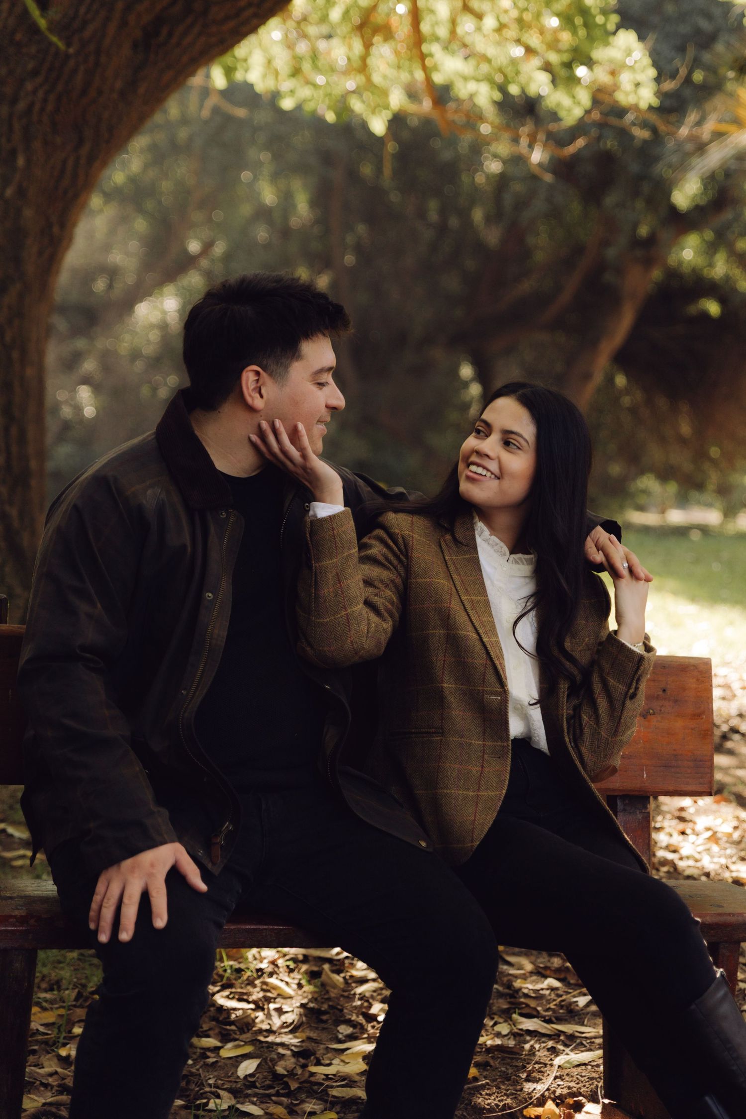 Smiling woman resting hand on mans face while sitting on park bench in fall.