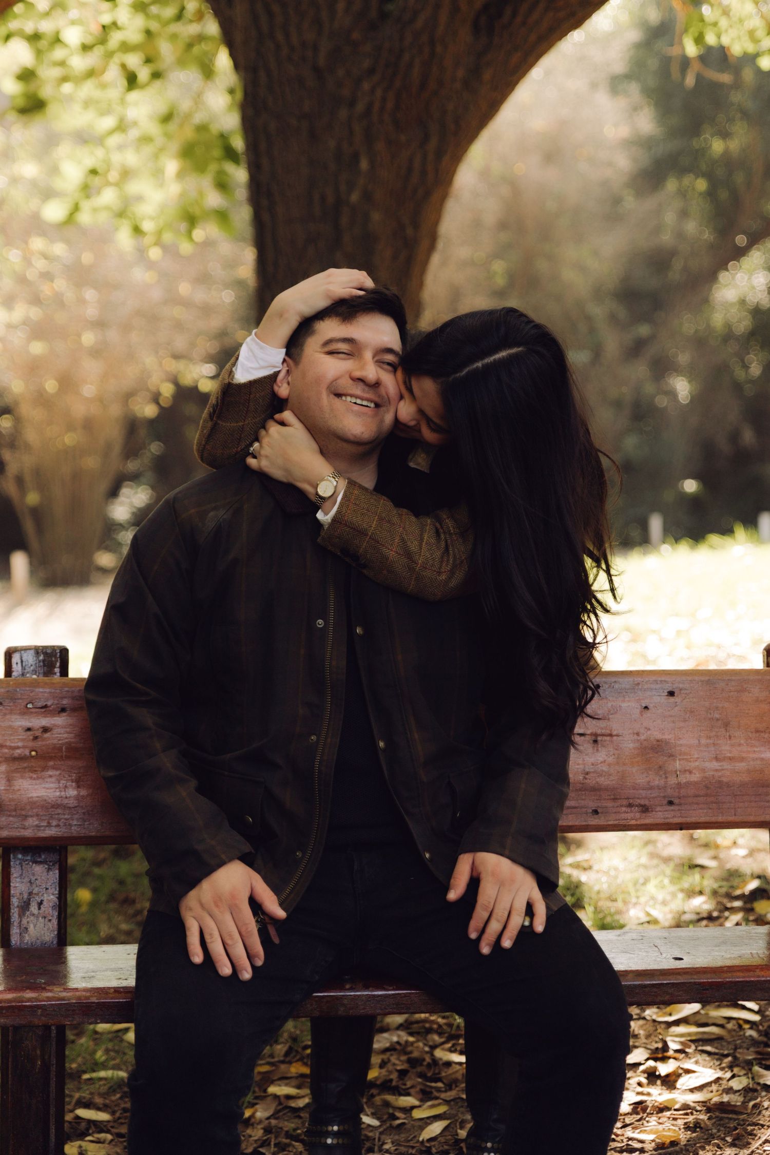 Laughing man being kissed on cheek by woman on a park bench in autumn.