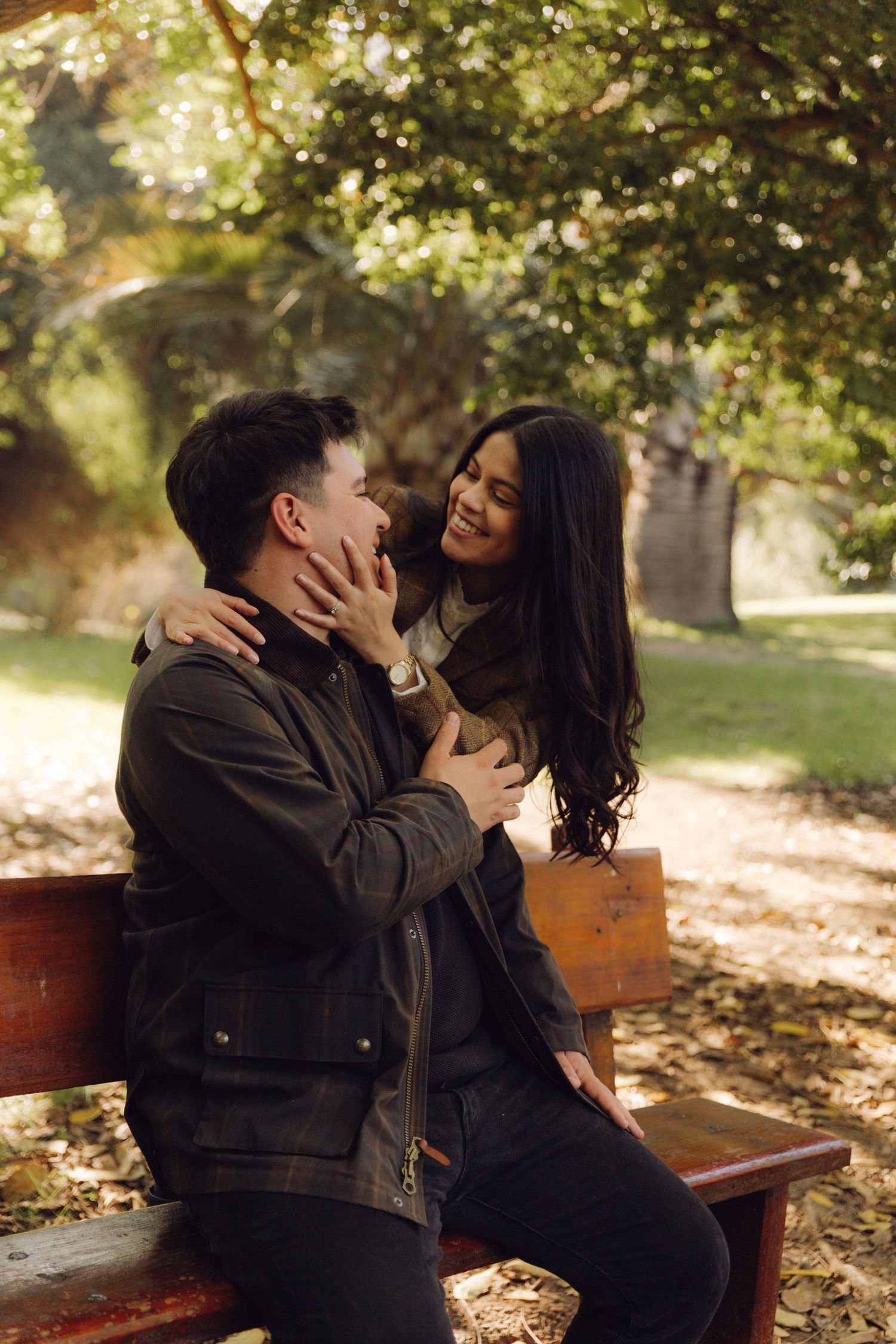 Young couple laughing and flirting together on a park bench surrounded by golden autumn foliage.