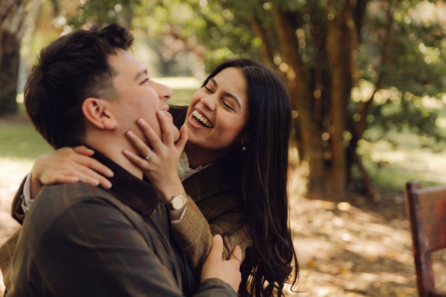 Happy couple sharing a joyful laugh outdoors in a sunlit autumn park, woman touching mans face.