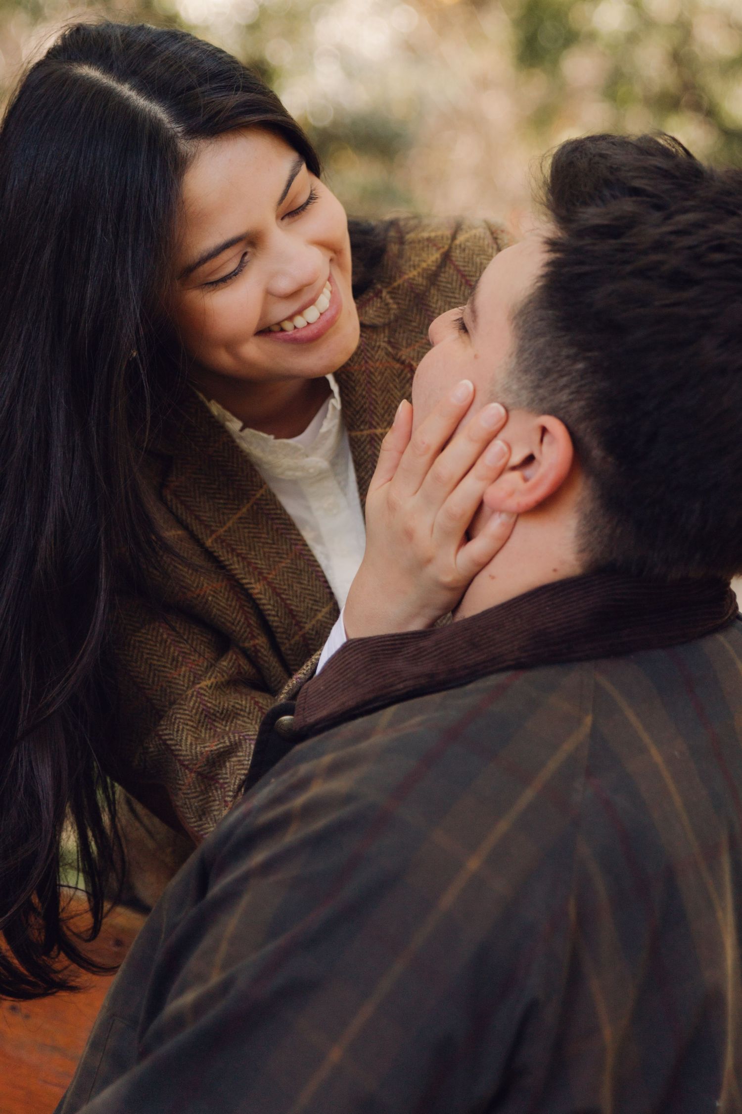 Smiling woman tenderly holding mans face while sharing an intimate moment outdoors in a park.