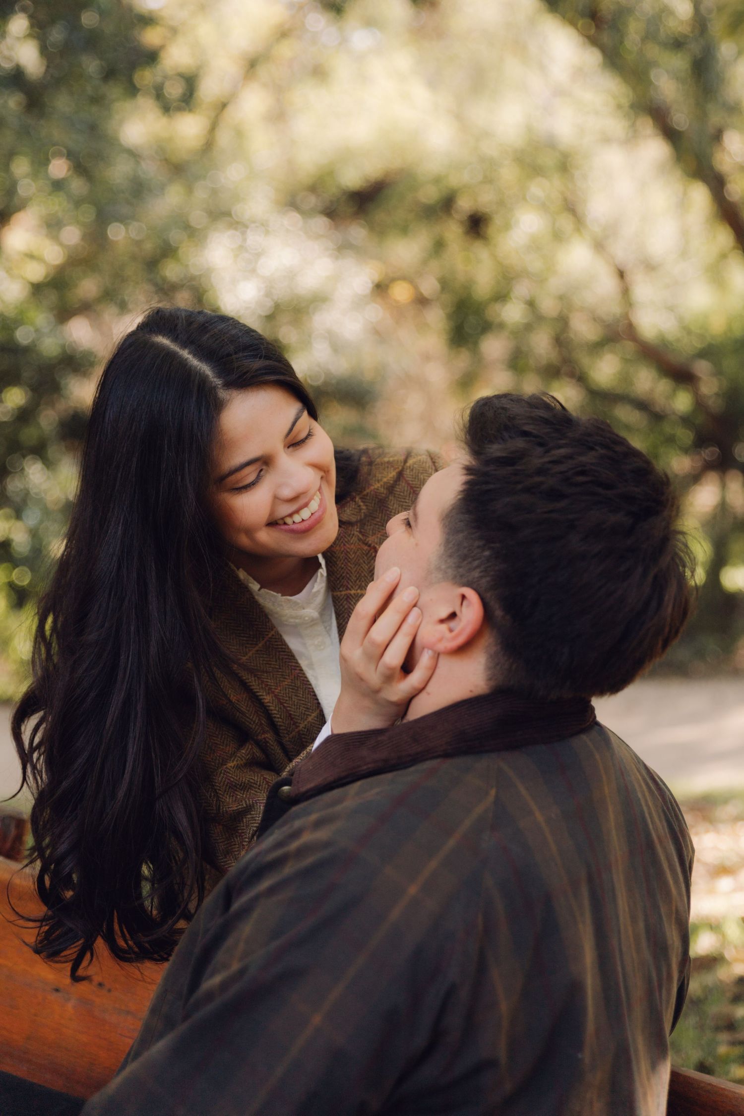 Cheerful couple sharing a warm smile on a park bench, woman gently touching mans cheek.