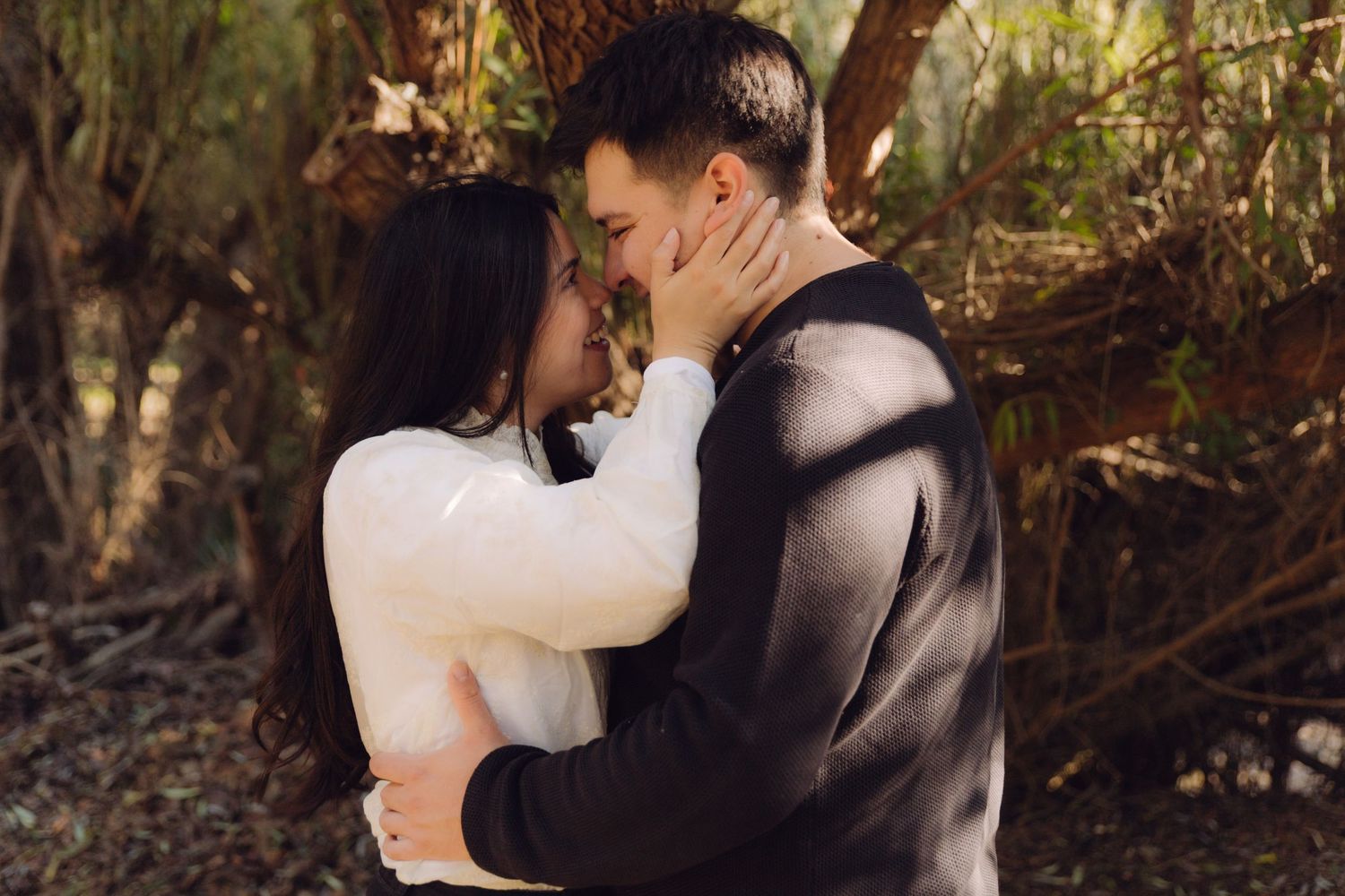 Romantic couple sharing an intimate almost-kiss moment surrounded by lush green foliage outdoors.