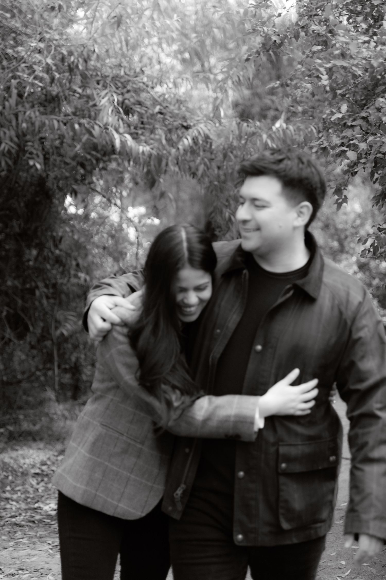 Black and white photo of laughing couple hugging while walking through an autumn park together.