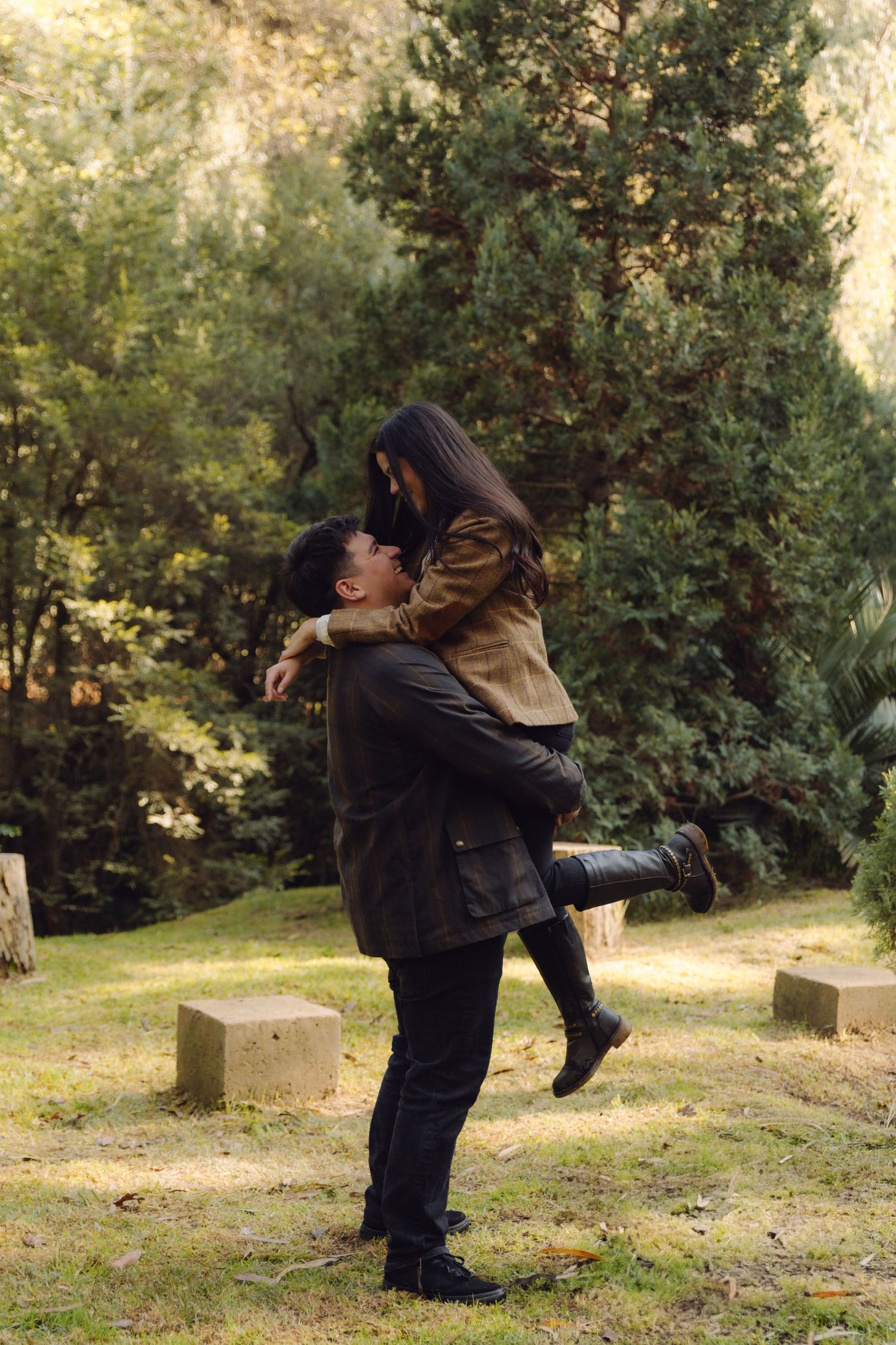 Joyful couple sharing a romantic moment as man lifts woman in a lush green outdoor park.