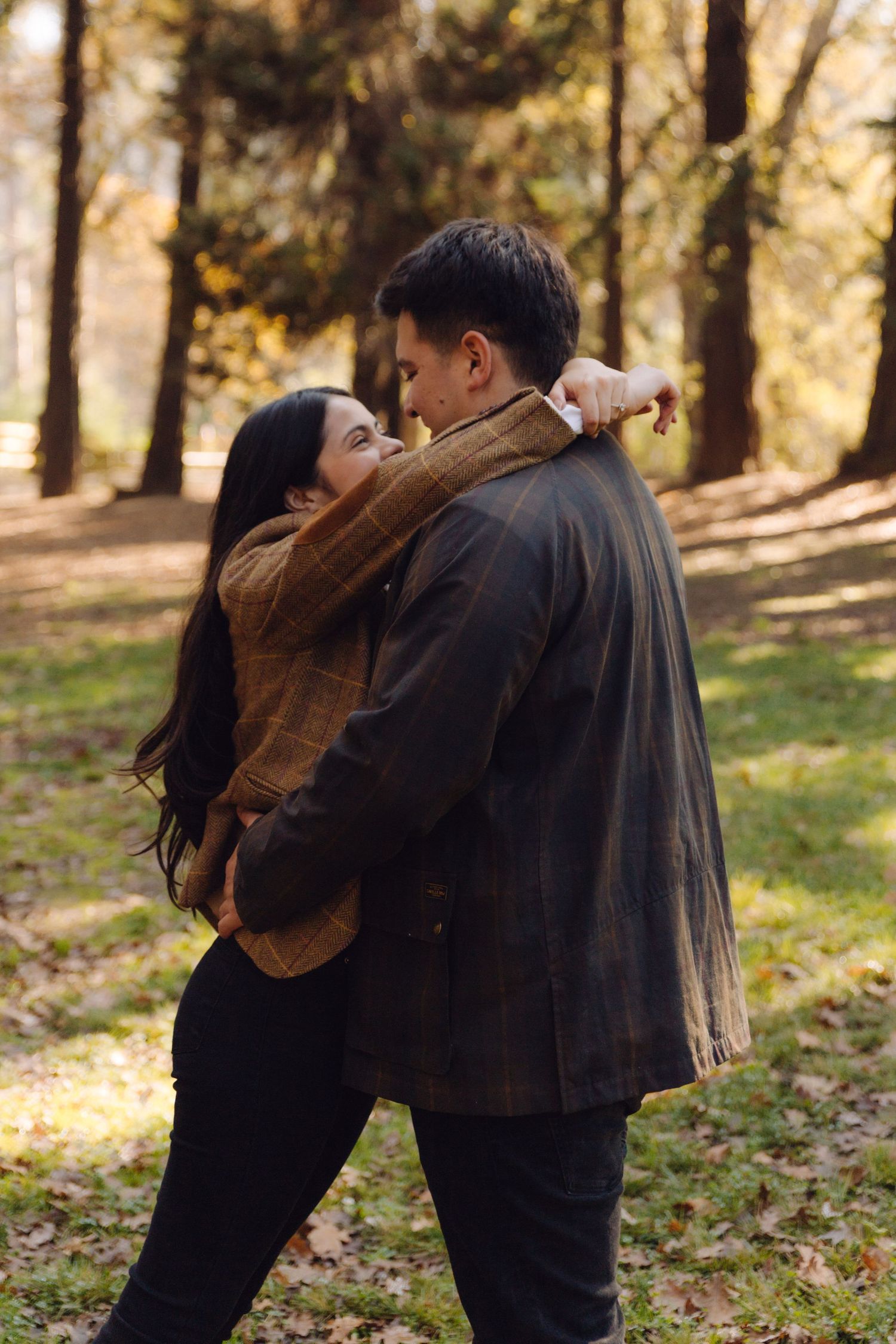 Couple embracing tenderly from behind in a golden autumn park with fallen leaves on the ground.