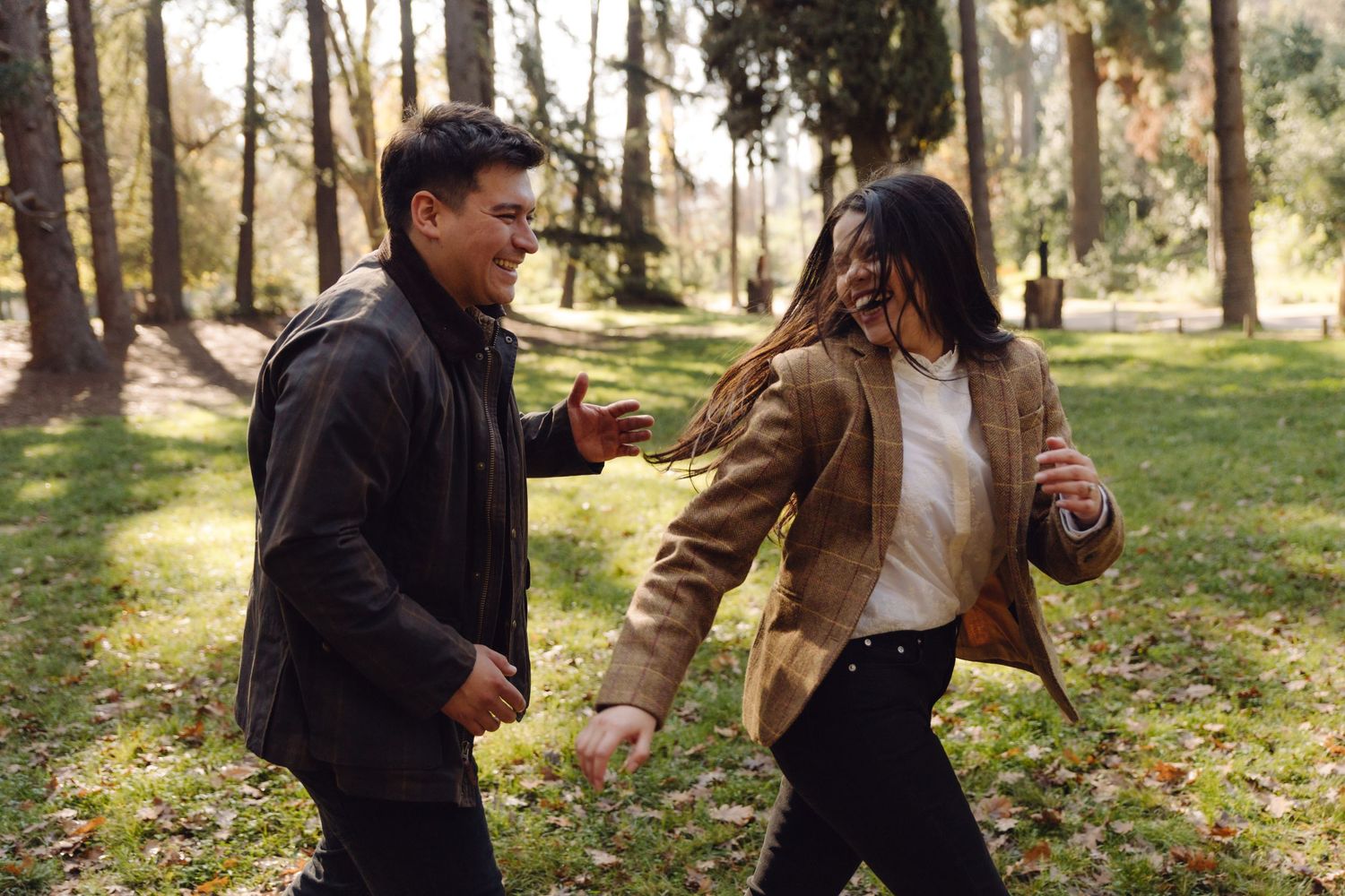 A happy couple dancing and playing together outdoors in a beautiful tree-lined park.