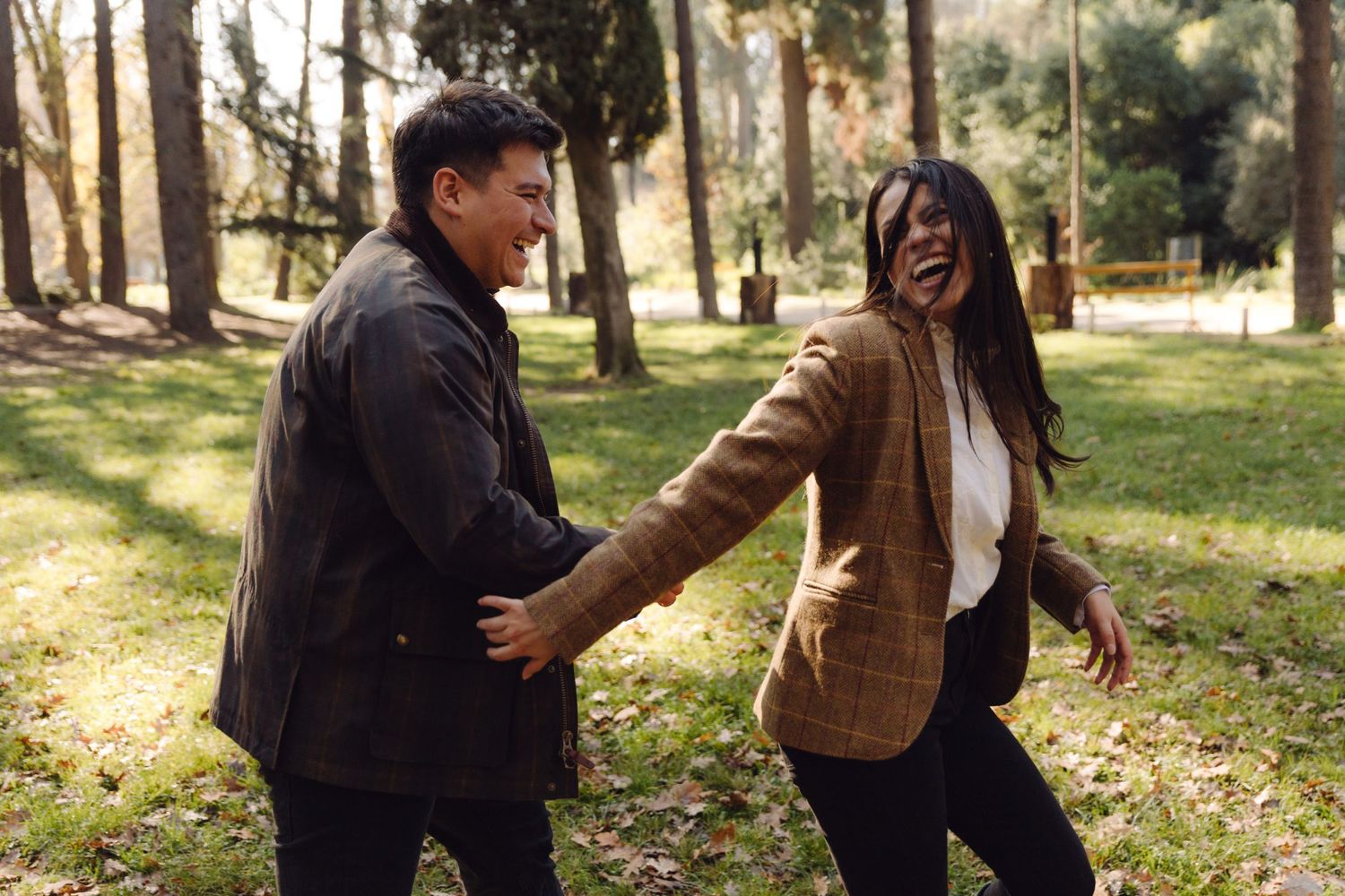 A joyful couple laughing and holding hands while walking through a sunlit autumn park.