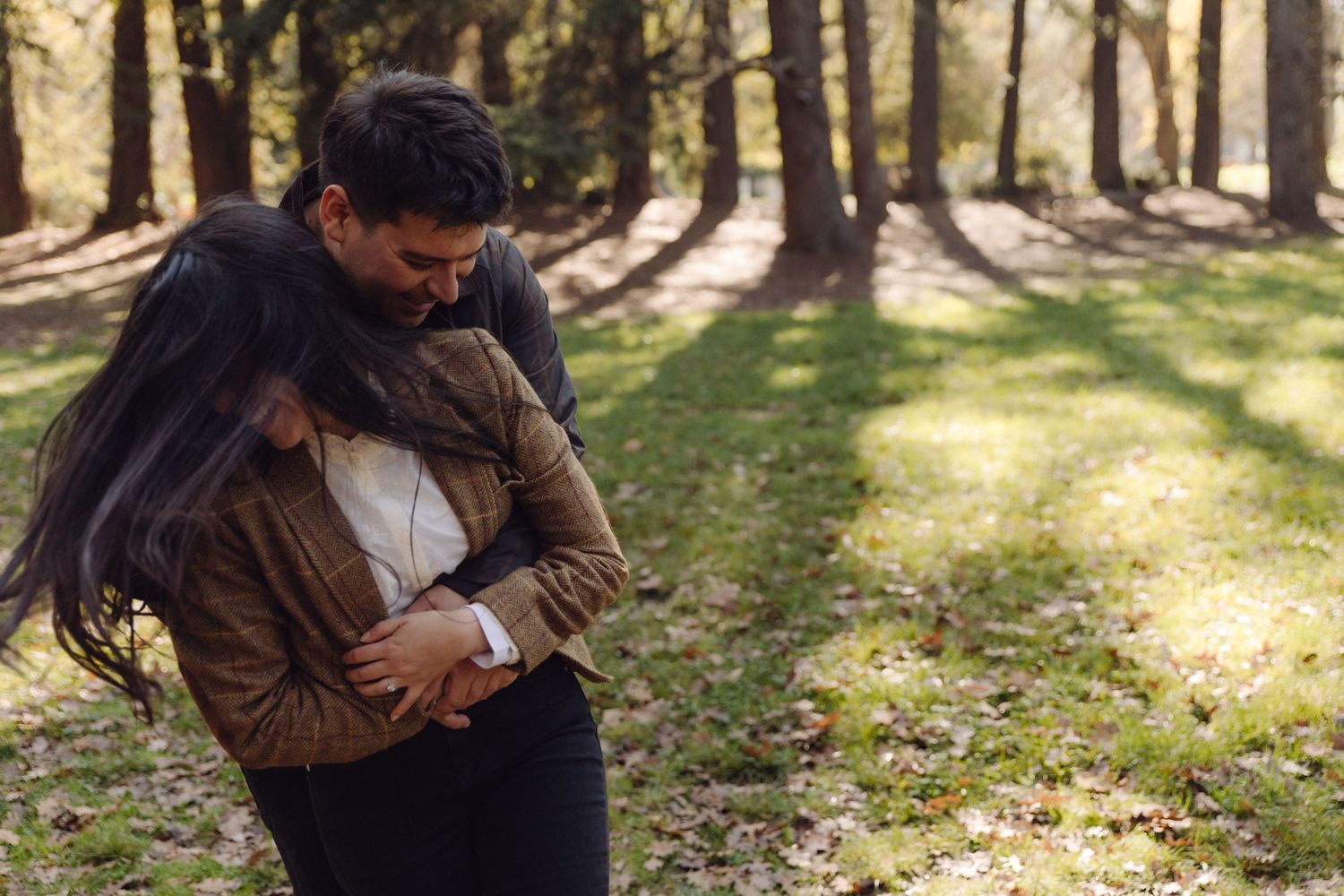 A romantic couple embracing closely in a sunlit forest park during autumn season.