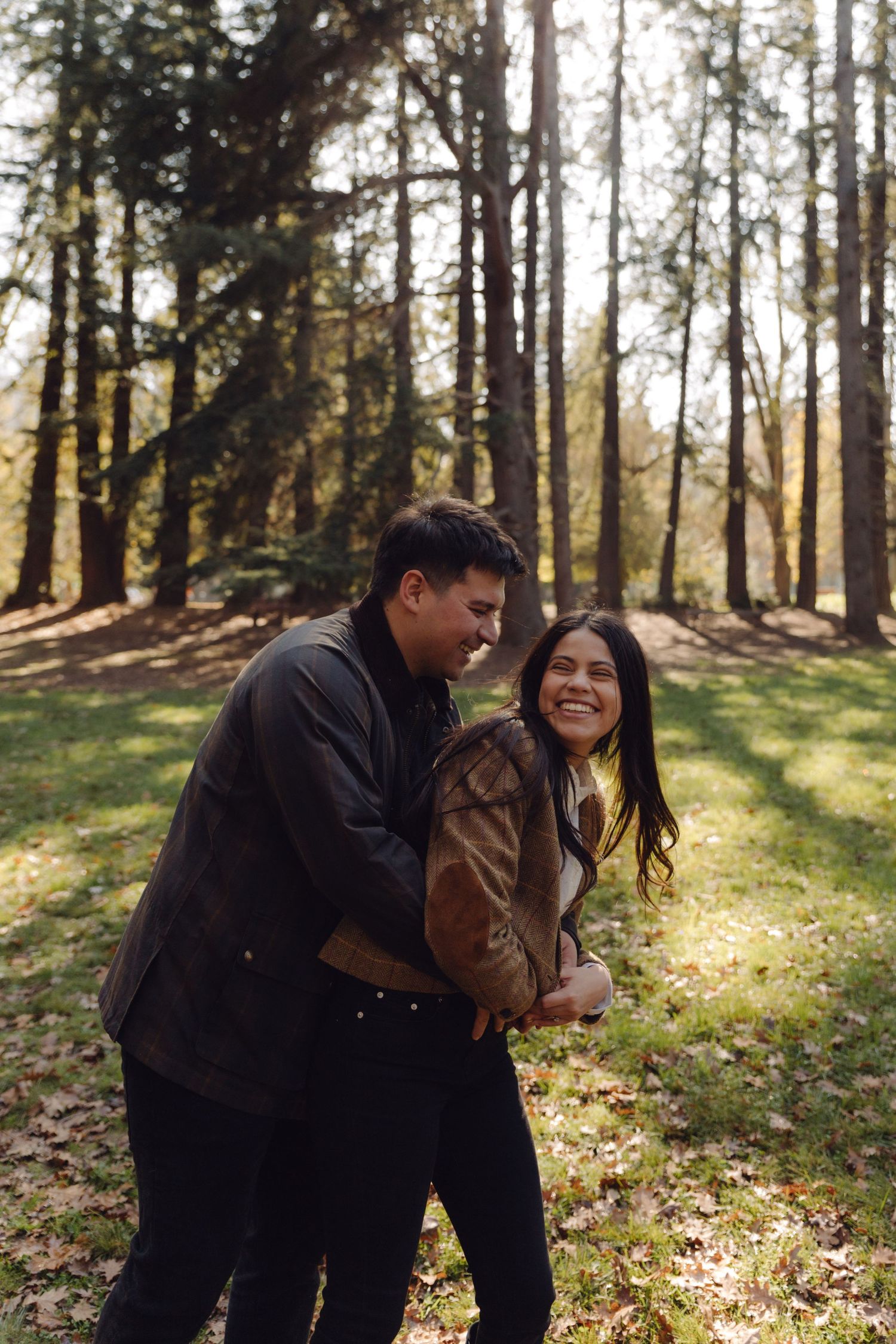 A smiling couple walking together through a sunny forest park in autumn foliage.