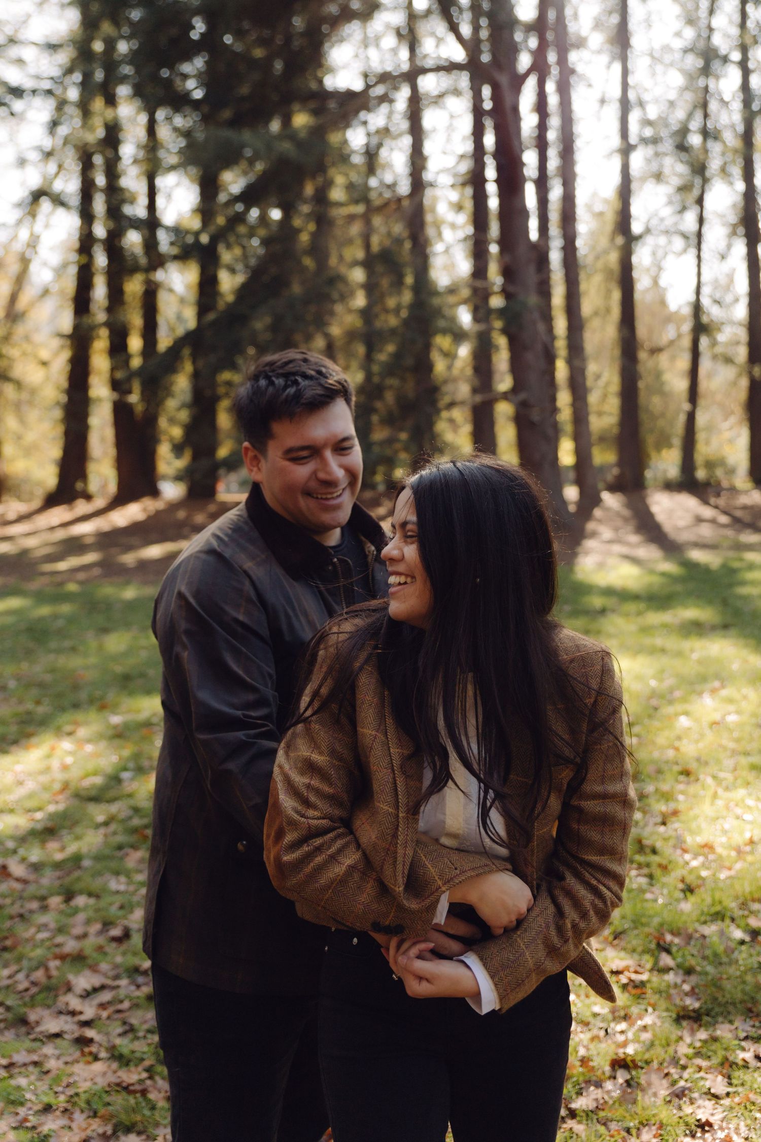 A happy couple holding each other and smiling in a beautiful sunlit autumn forest.
