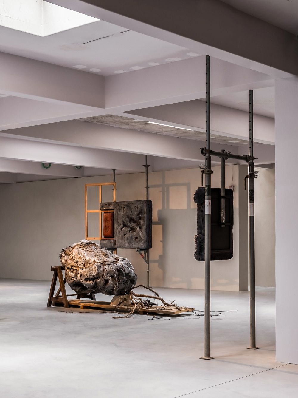 Contemporary art installation in gallery with large organic sculpture on wooden frame and metal pole structure.