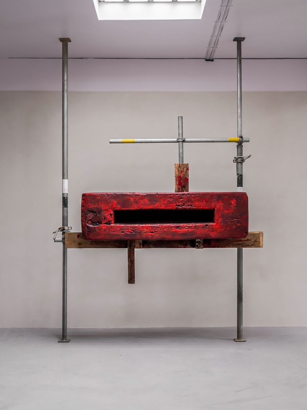 Red weathered metal mailbox mounted on steel pipes and wooden beam in a minimalist gallery installation artwork.