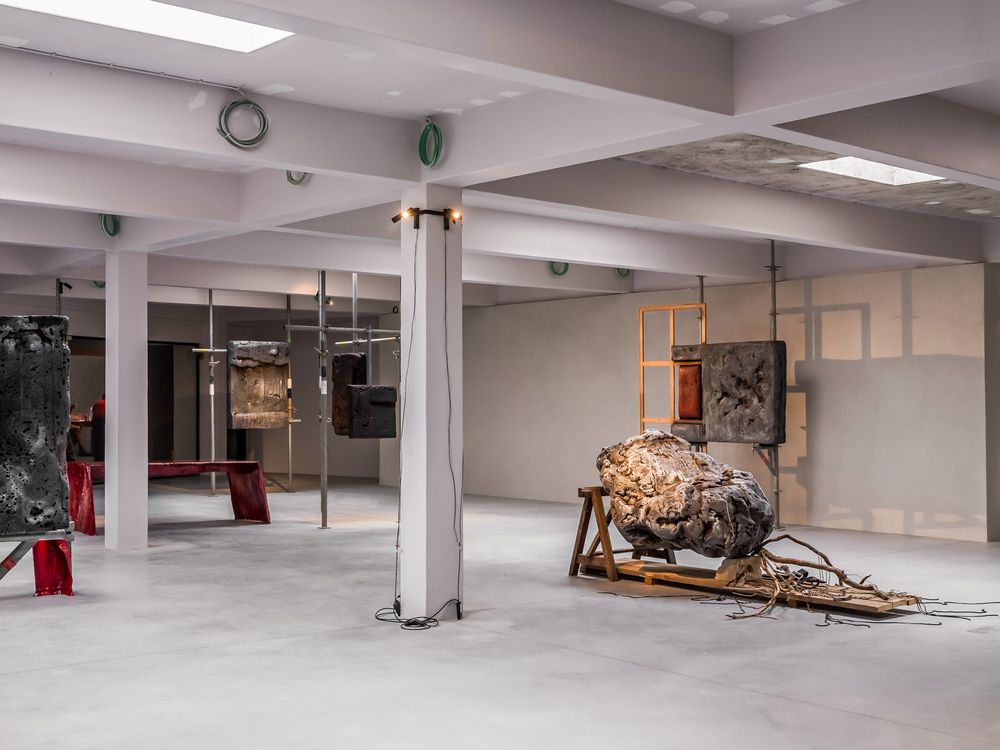 Industrial art installation in a spacious gallery with sculptures, hanging objects, and textured walls under fluorescent lighting.